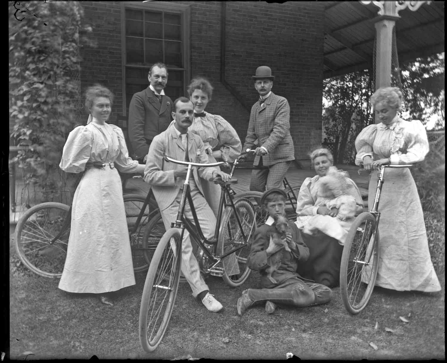 Group portrait taken on the porch of the Patteson family home in Eastwood. The group is posing with bicycles.