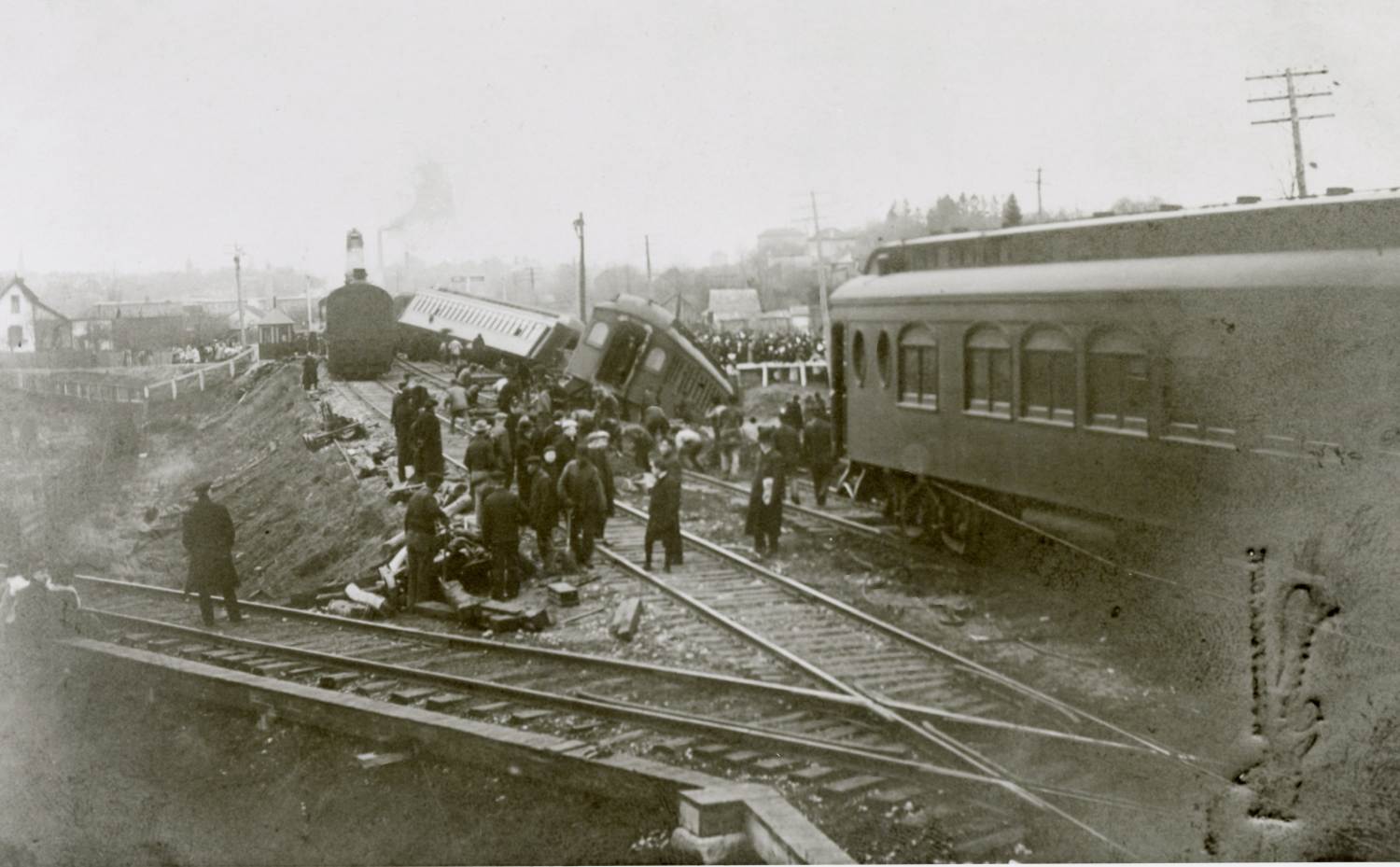 A photo of the Lehigh Express train derailment. The train cars are off the rails. A large group of people are gathered around the train, with a crowd standing in the distance. Buildings can also be seen in the distance as a town is nearby.