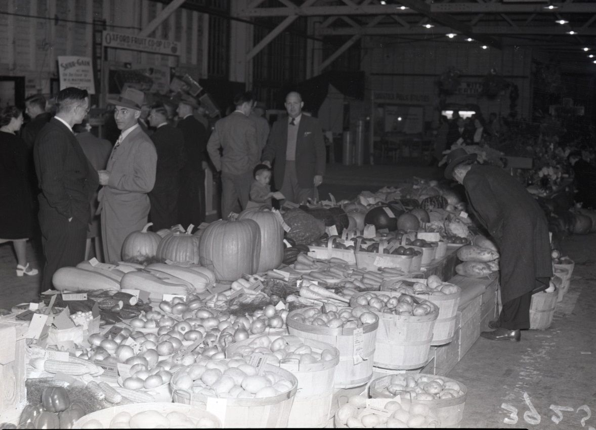 Group of people looking at a display of large vegetable and fruits inside a building at the Woodstock Fair.