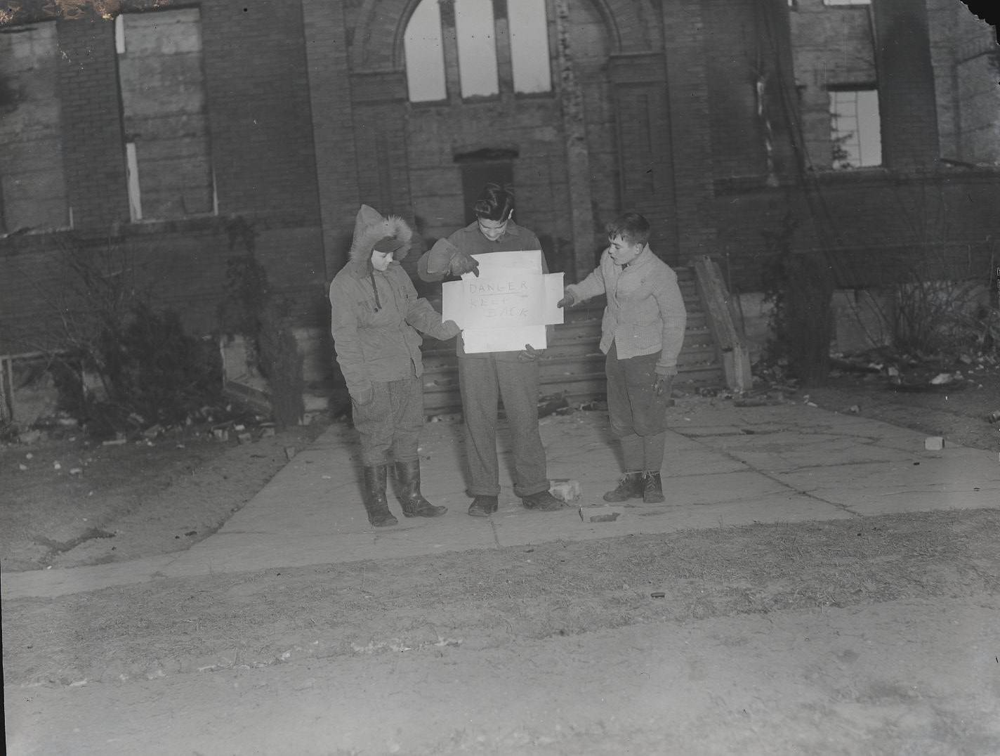 Three young boys holding a sign that reads “Danger Keep Back” in front of the Princeton Continuation School following a fire that destroyed the building. 