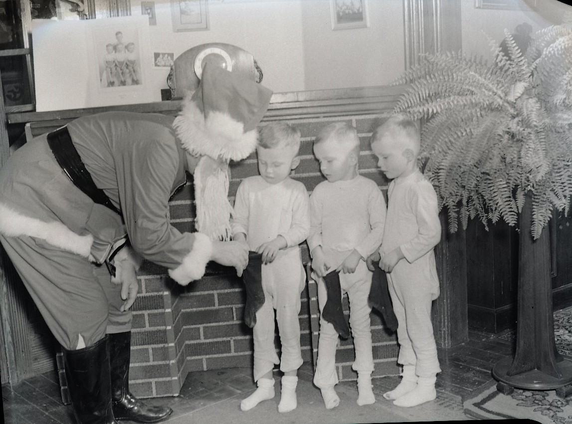 Three twin boys holding stocking out to Santa Claus.