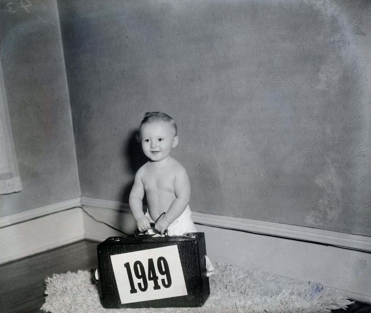 Toddler in a diaper holding a suitcase that says 