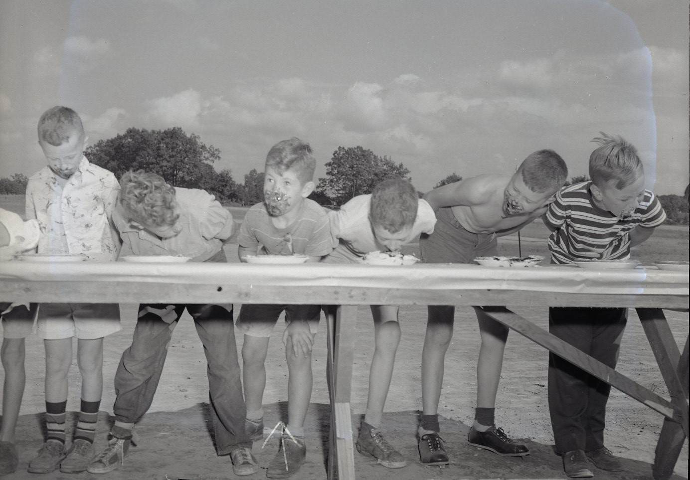 Group of boys standing along a table eating pie for a contest.