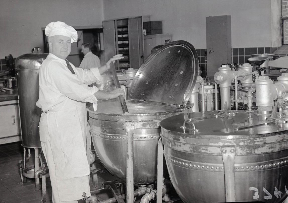 Chef wearing a chef hat and uniform stirring a large vat of hot spaghetti at the Ontario Hospital