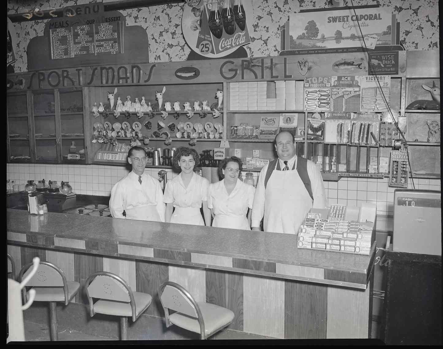 Four staff members, two women and two men, are wearing uniforms and standing behind the counter at the 