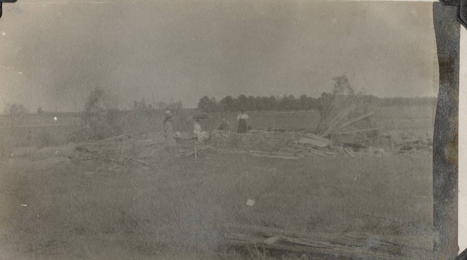 A group people standing in a farm field with debris left from a tornado. Black and white photo.