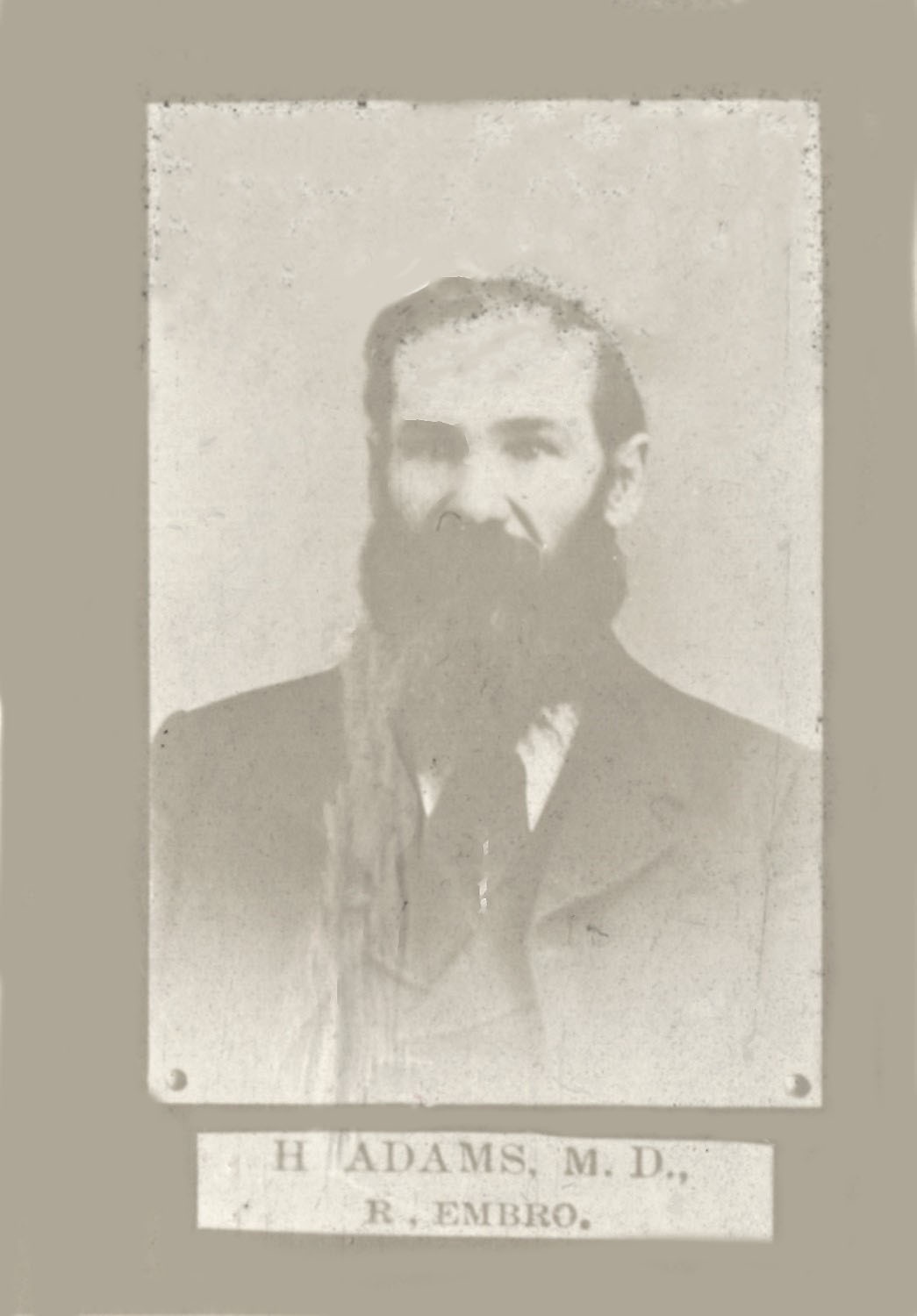 A black and white portrait of Dr. Henry Adams, his face is covered in a thick beard and he is wearing a suit,