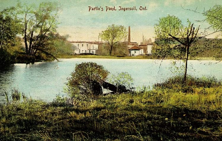 A postcard featuring a photo of Partlo's Pond in Ingersoll, Ontario. White buildings can be seen in the background.