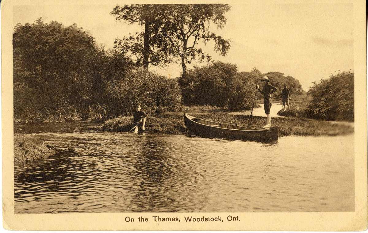 Young men standing on the banks of the Thames River with their canoe.