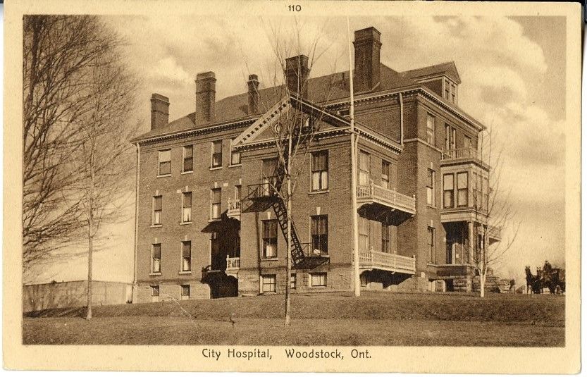 Postcard featuring the Woodstock City Hospital in the early 1900s. The hospital is several storeys tall, built of brick, with balconies on the front. A horse-drawn carriage is pulling up to the front of the building.