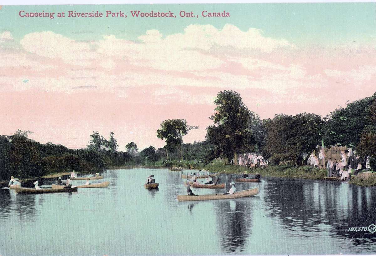 A postcard featuring people canoeing at Riverside Park in Woodstock, Ontario. People are standing long the river banks watching the people in canoes.