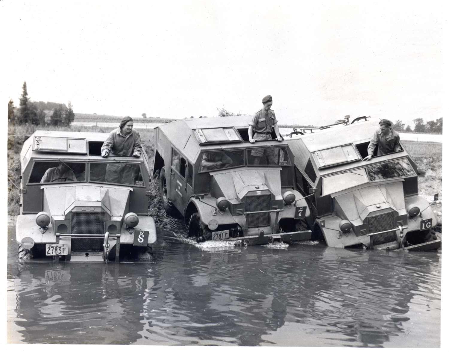 Men are driving three universal carrier vehicles into the Thames River.