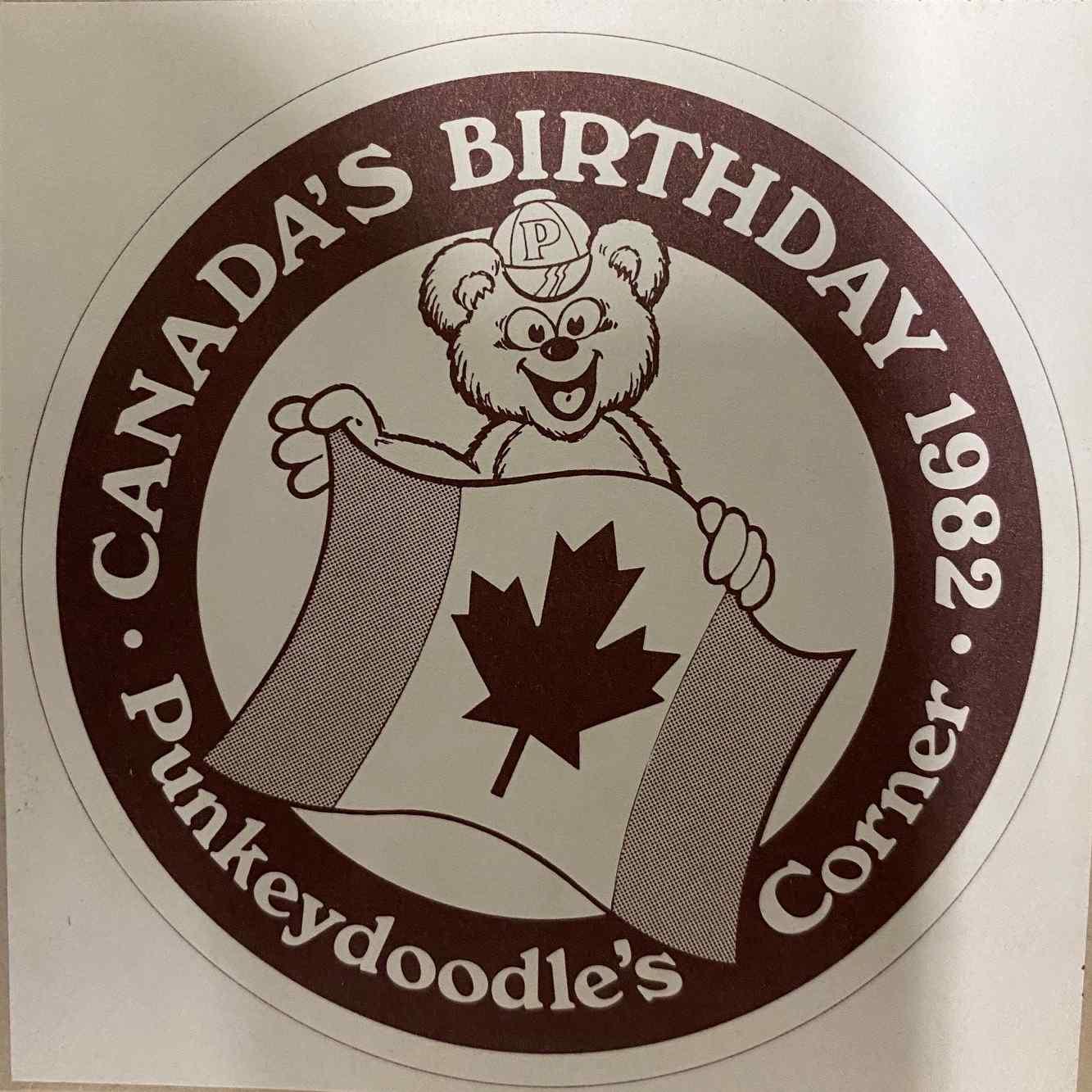 Punkeydoodle's Corner Canada Day celebration logo, from 1982, featuring a sketch of a cartoon bear wearing a baseball cap with a 