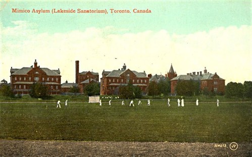 Mimico Asylum Postcard, multiple red brick building with people wearing white standing out front.